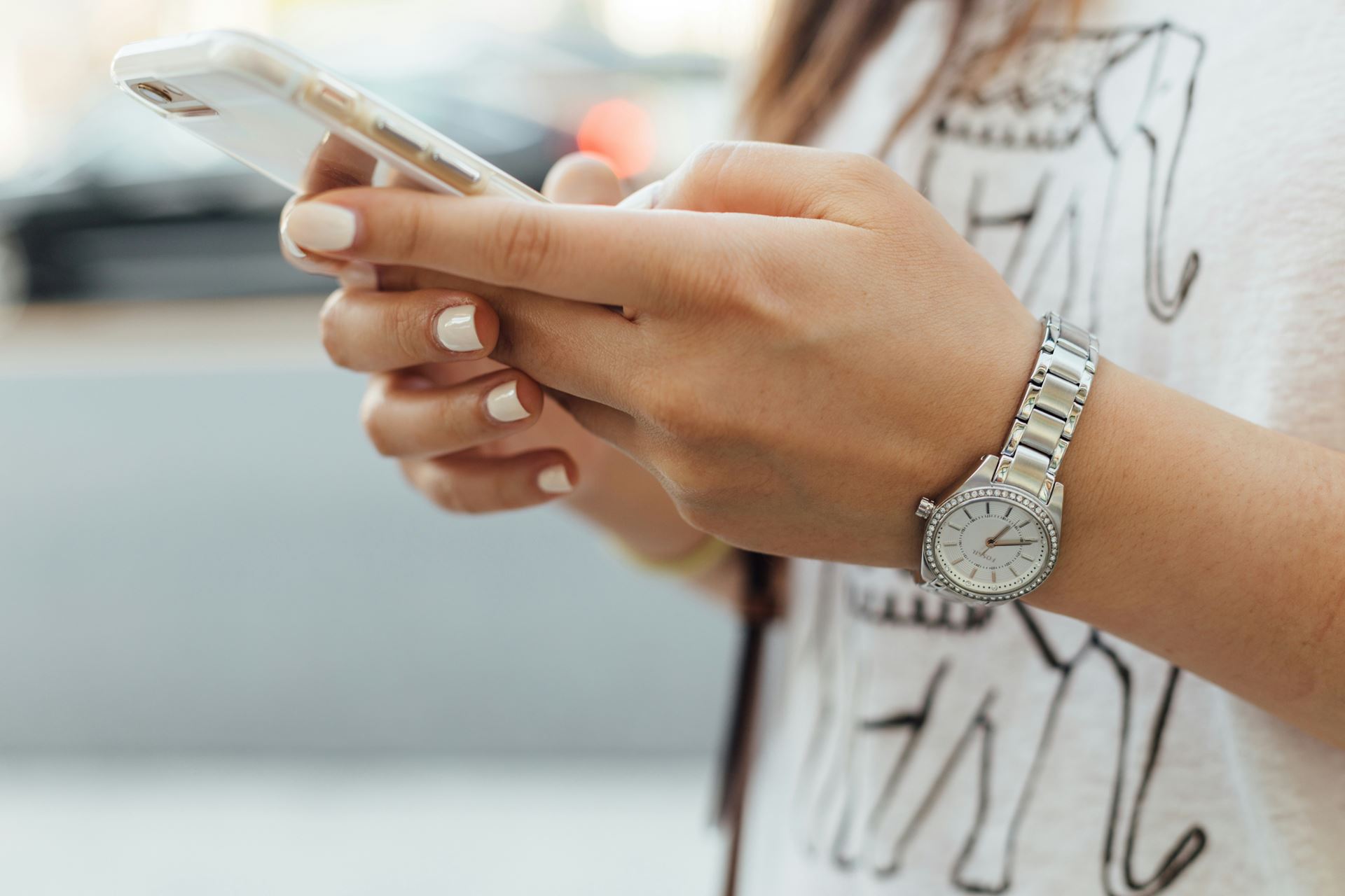lady checking her mobile phone with manicured nails and a silver coloured watch